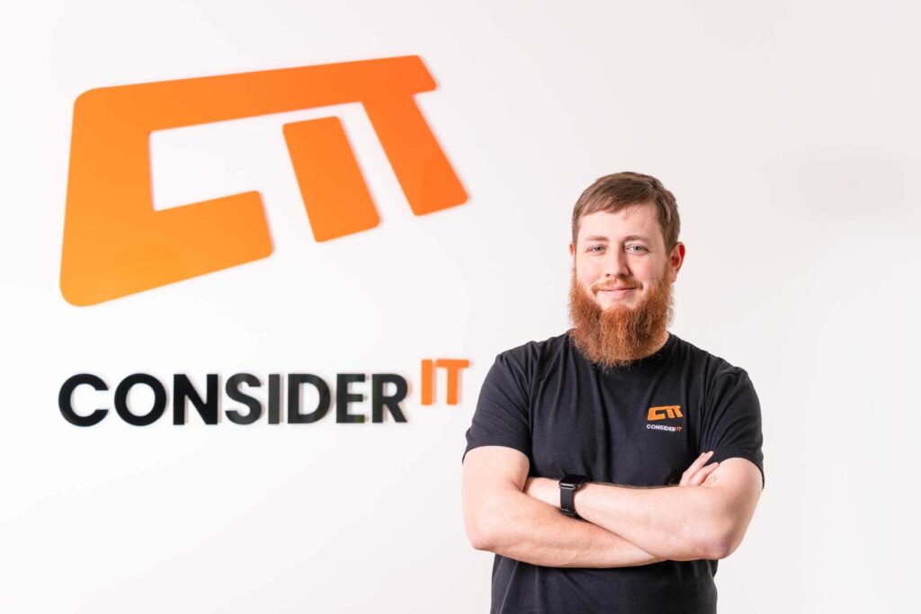 A picture of Gary Clark one of Consider IT's IT Technicians standing by the Consider IT logo.