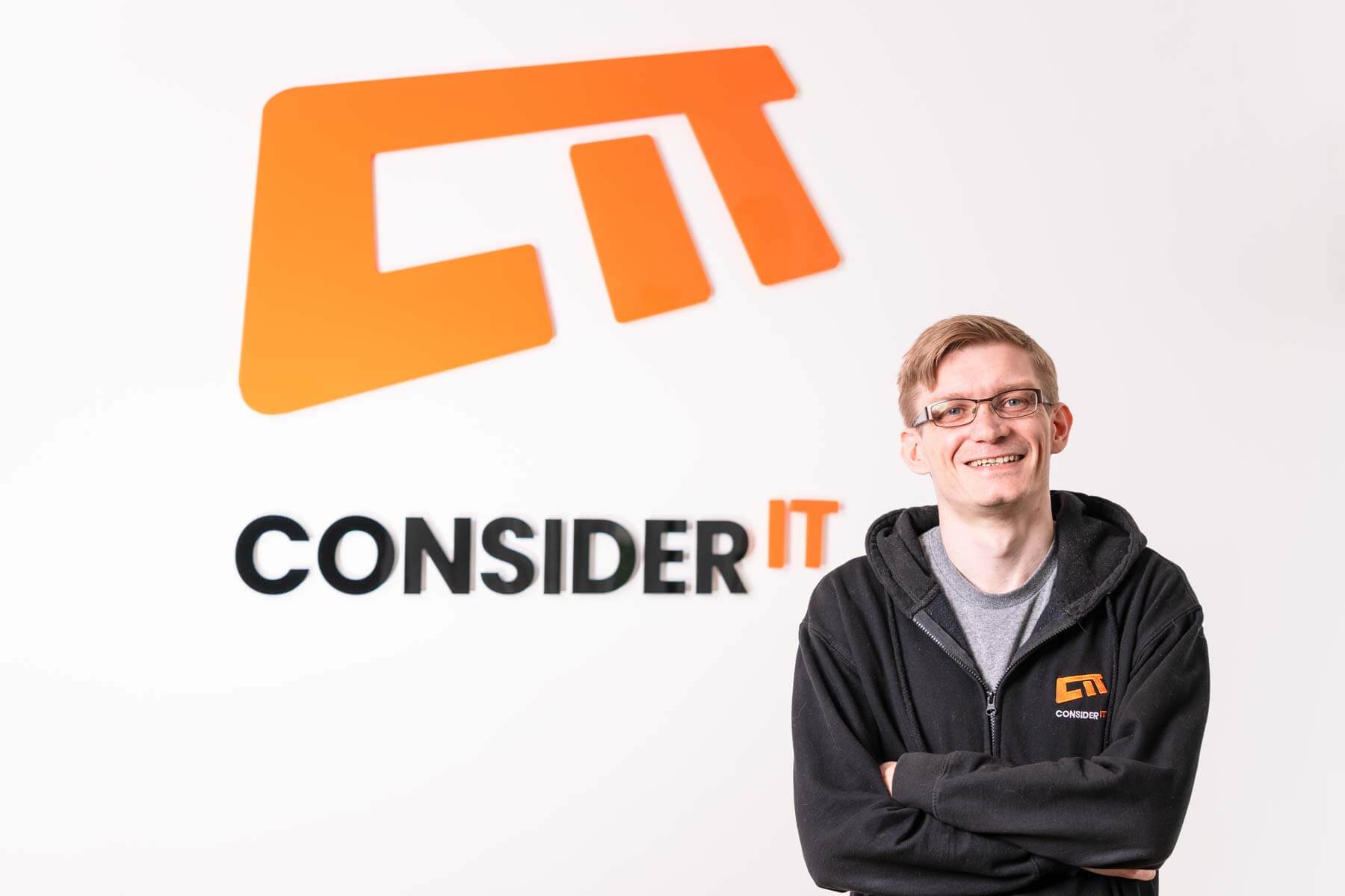 A picture of Stephen Whitelaw one of Consider IT's IT Technicians standing by the Consider IT logo.