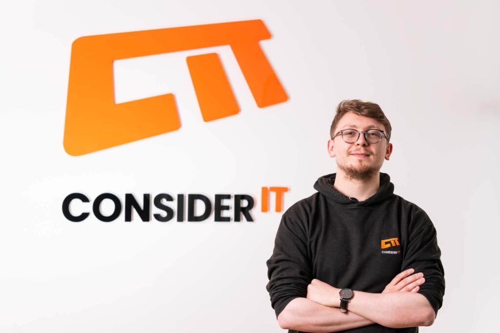 A picture of Brad Vernon one of Consider IT's IT Technicians standing by the Consider IT logo.