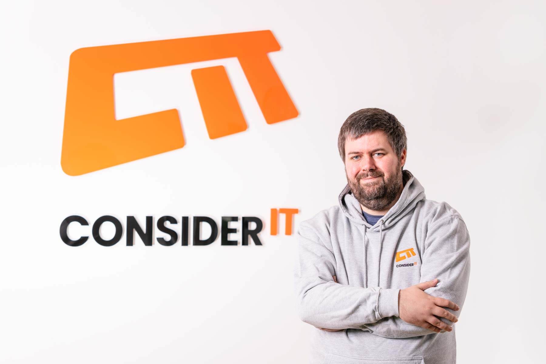 A picture of Ryan Shiells one of Consider IT's IT Technicians standing by the Consider IT logo.