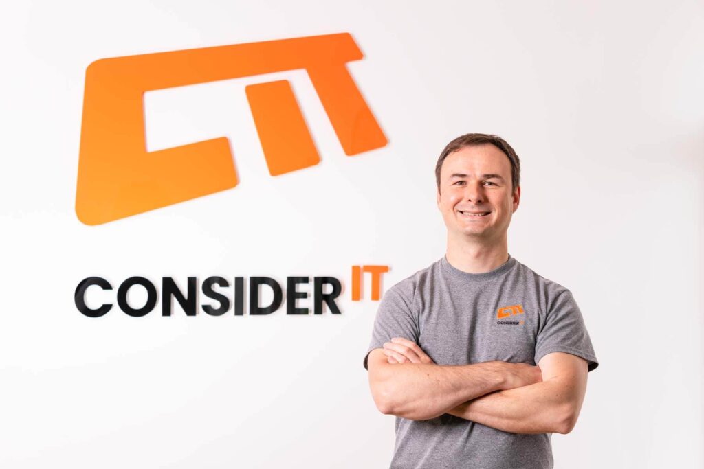 A picture of Marcin Masternak one of Consider IT's IT Technicians standing by the Consider IT logo.