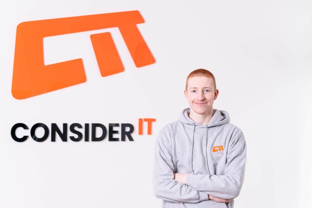 A picture of Lewis Grisenthwaite one of Consider IT's IT Technicians standing by the Consider IT logo.