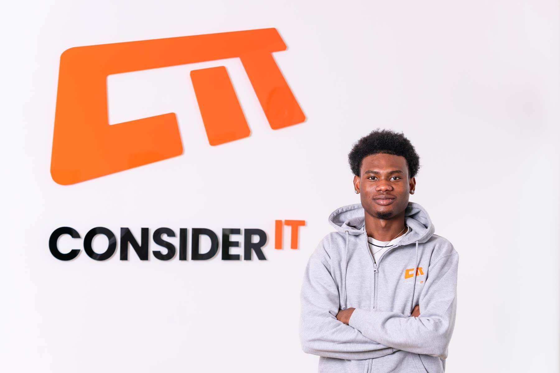 A picture of Ayoola Ifesanya one of Consider IT's IT Technicians standing by the Consider IT logo.