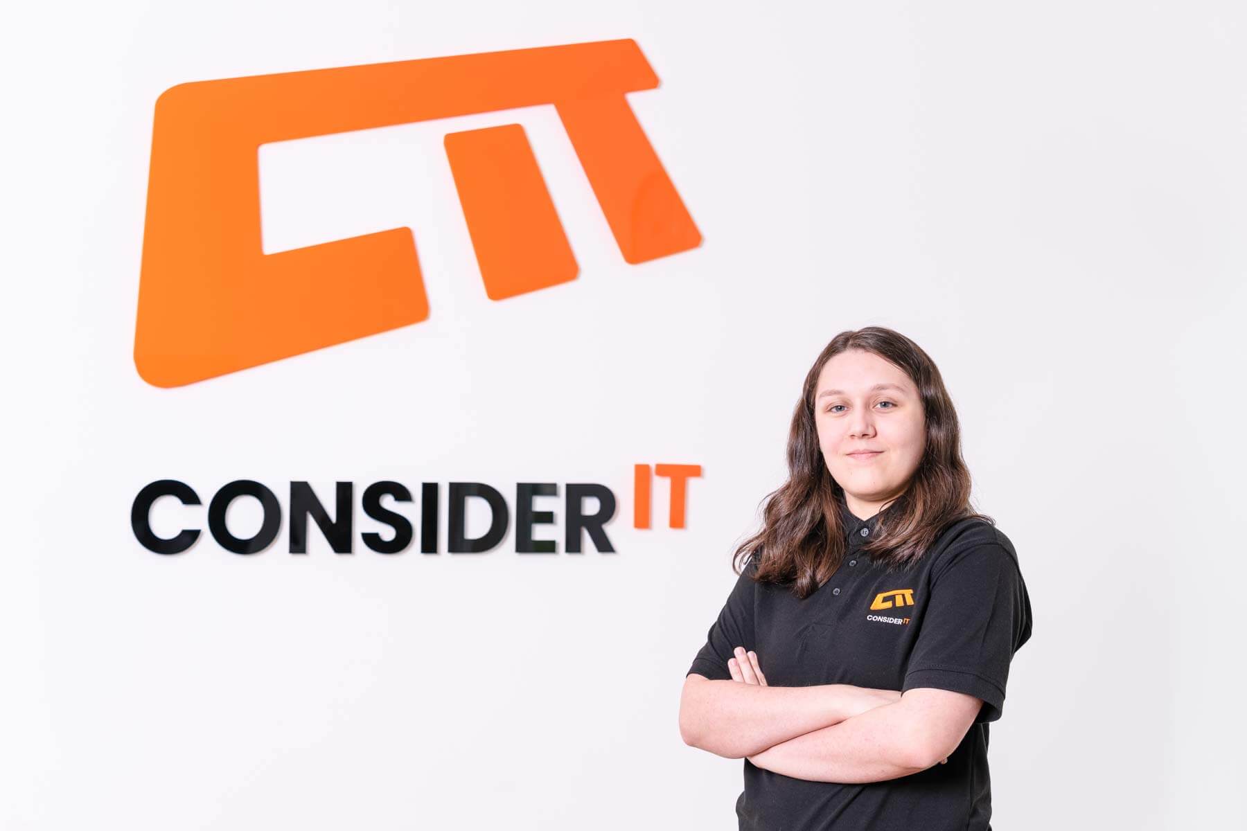 A picture of Leah Morris one of Consider IT's IT Technicians standing by the Consider IT logo.