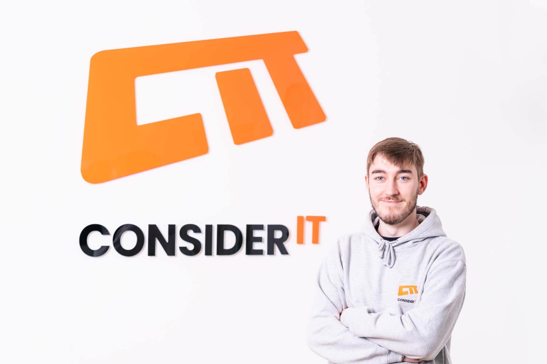 A picture of Lewis Elder one of Consider IT's IT Technicians standing by the Consider IT logo.